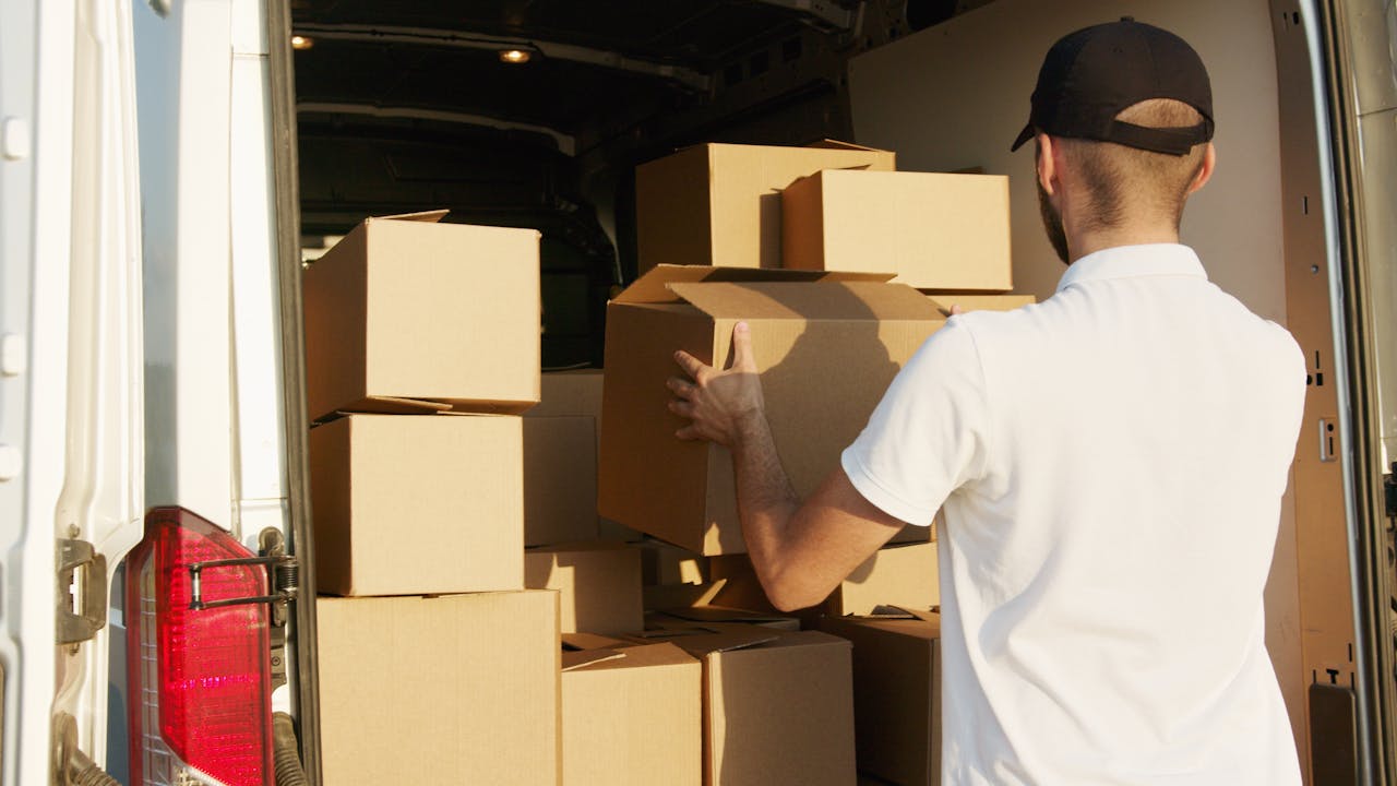 about-us Courier arranging cardboard boxes in a delivery van during daytime.